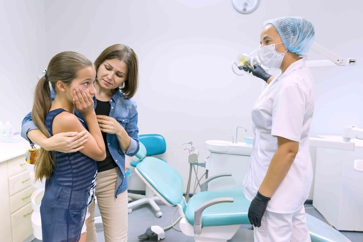 Child with dental pain and parent speaking to an emergency dentist for kids