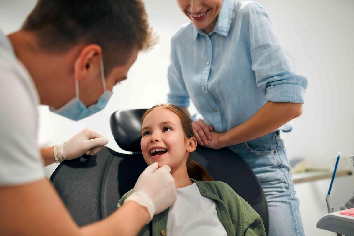 Pediatric dentist examining a child while a parent offers support during a dental visit