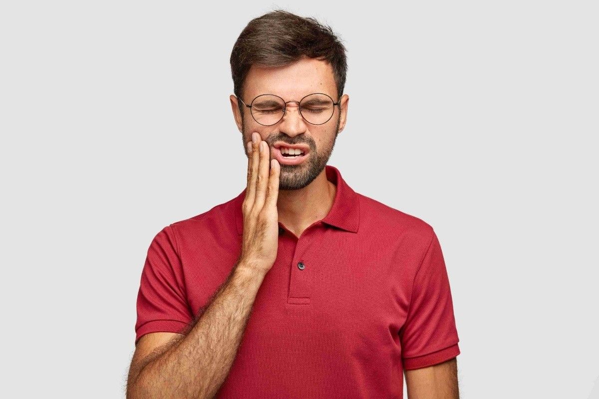 Person holding their cheek due to severe tooth pain during a dental emergency.